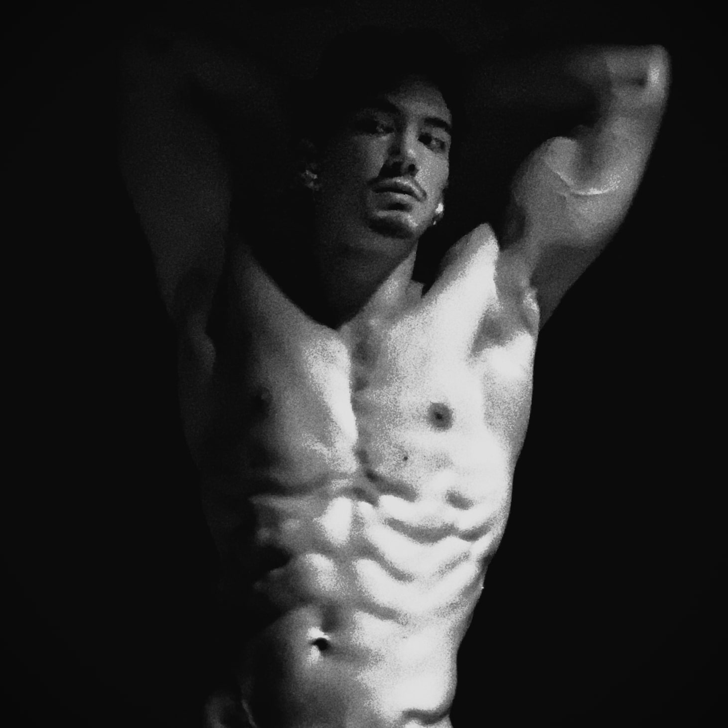 Andrew Valentine with both arms raised behind his head, lit from above against a dark ground.