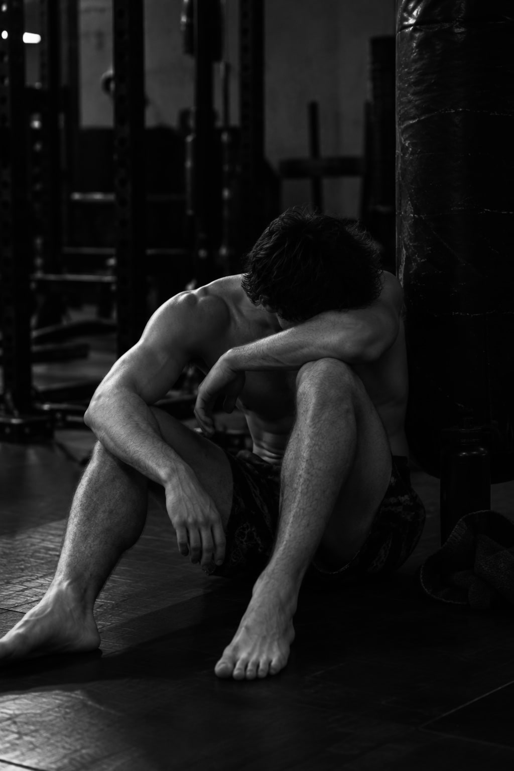 Andrew Valentine sitting on a gym floor against a heavy bag between rounds, head down on his forearm.