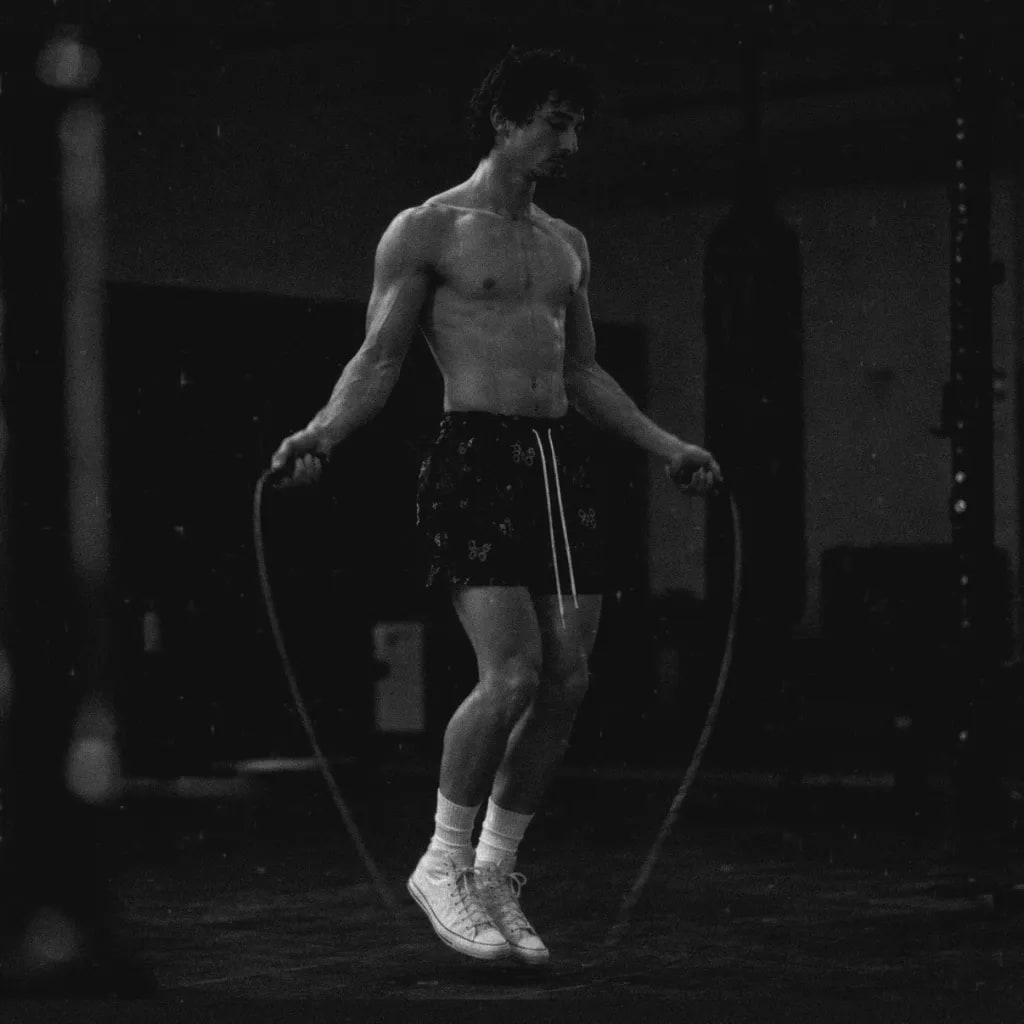 Andrew Valentine skipping rope in a dim gym, both feet off the floor.